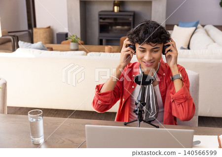 Man speaking into microphone wearing headphones, using laptop at table in living room Man speaking into microphone wearing headphones, using laptop at table in living room 140566599