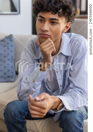 Man wearing wristwatch sitting on sofa at home resting chin beside pillow, framed artwork 140566600