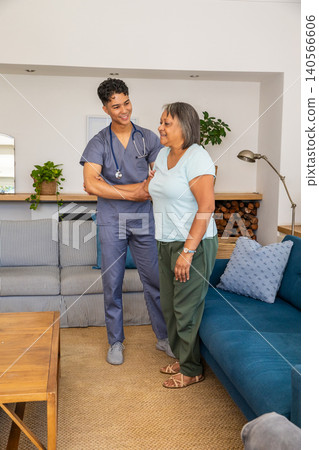 Asian male caregiver supporting senior woman standing by sofa in living room with stethoscop Asian male caregiver supporting senior woman standing by sofa in living room with stethoscop 140566606