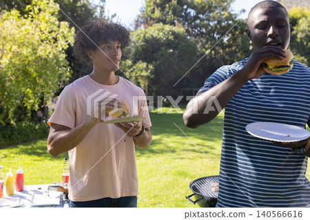 Diverse male friends grilling burgers on charcoal grill in garden near table with condiments Diverse male friends grilling burgers on charcoal grill in garden near table with condiments 140566616