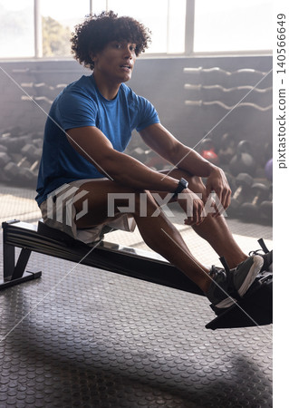 African American man rowing on rowing machine in gym featuring dumbbells kettlebells and smartwatch African American man rowing on rowing machine in gym featuring dumbbells kettlebells and smartwatch 140566649