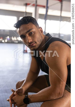 Asian male resting on bench at gym wearing digital watch, surrounding pull-up rig and dumbbells Asian male resting on bench at gym wearing digital watch, surrounding pull-up rig and dumbbells 140566651