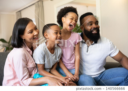 Family sitting on gray sofa in living room smiling with potted plant and curtains Family sitting on gray sofa in living room smiling with potted plant and curtains 140566666