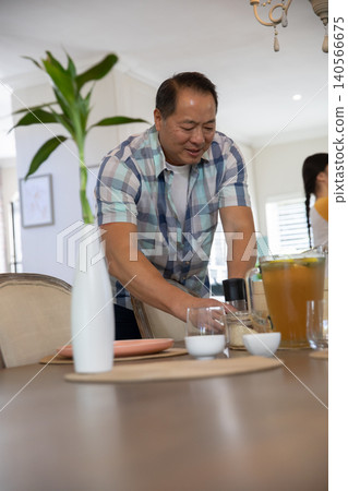 Asian father and daughter arranging placemats, carafe, glasses on dining table in dining room 140566675