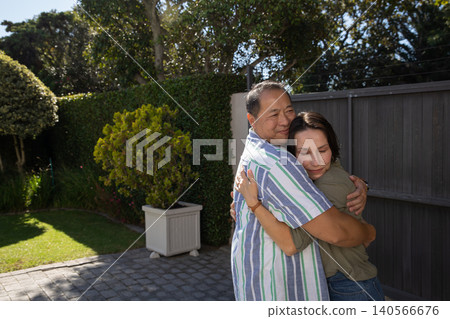 Diverse couple hugging on stone paver patio with trimmed shrub and fence in sunlight Diverse couple hugging on stone paver patio with trimmed shrub and fence in sunlight 140566676