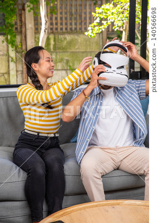 Indian and chinese couple placing vr headset on head while sitting on sofa on patio Indian and chinese couple placing vr headset on head while sitting on sofa on patio 140566698