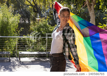 Female standing and smiling on deck near benches and metal railing with rainbow flag, copy space 140566703
