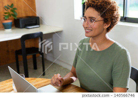 African american woman sitting at round table with glass of water using laptop in home African american woman sitting at round table with glass of water using laptop in home 140566746