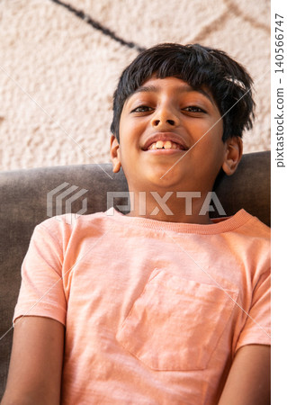 Preteen indian boy reclining on couch cushion in living room, wearing peach shirt and smiling Preteen indian boy reclining on couch cushion in living room, wearing peach shirt and smiling 140566747