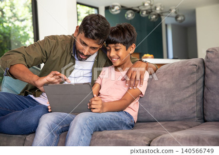 Asian father and son sitting on sectional sofa using tablet in home living room Asian father and son sitting on sectional sofa using tablet in home living room 140566749