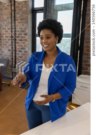 Mid adult african american woman pointing at window at desk in office Mid adult african american woman pointing at window at desk in office 140566756