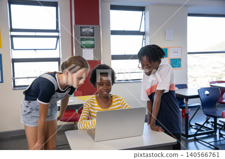 Diverse schoolchildren collaborating around silver laptop at classroom desk Diverse schoolchildren collaborating around silver laptop at classroom desk 140566761