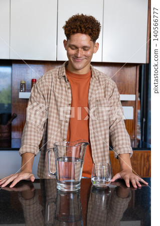Man standing behind granite island in kitchen, leaning on counter near glass pitcher, tumbler Man standing behind granite island in kitchen, leaning on counter near glass pitcher, tumbler 140566777