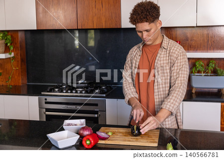 Man slicing eggplant with knife on wooden cutting board at kitchen island, copy space Man slicing eggplant with knife on wooden cutting board at kitchen island, copy space 140566781