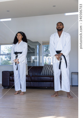 Diverse training partners practicing martial arts stance in living room wearing gis and belts Diverse training partners practicing martial arts stance in living room wearing gis and belts 140566783