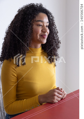 African american woman sitting at tabletop on woven-back chair in white room, folding hands 140566784