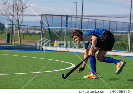 Teenage boy in jersey leaning forward gripping field hockey stick on green turf, copy space Teenage boy in jersey leaning forward gripping field hockey stick on green turf, copy space 140566830