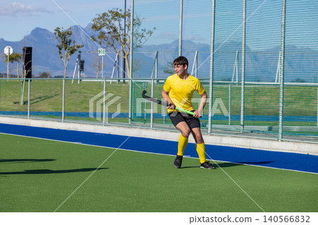 Teenage boy in yellow jersey dribbling ball with hockey stick on turf next to fence, copy space Teenage boy in yellow jersey dribbling ball with hockey stick on turf next to fence, copy space 140566832
