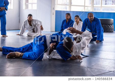 Diverse martial arts class in gis practicing ground grappling on mats in gym with tires Diverse martial arts class in gis practicing ground grappling on mats in gym with tires 140566834