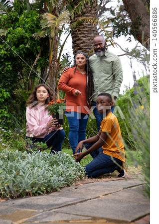 African american senior couple gardening with diverse kids tending pot of blooms on walkway 140566886