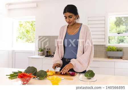 Adult Asian woman chopping yellow bell pepper using chef knife on cutting board at kitchen counter Adult Asian woman chopping yellow bell pepper using chef knife on cutting board at kitchen counter 140566895