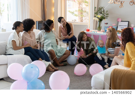 Diverse female friends celebrating baby shower in living room with balloons, baby, camera Diverse female friends celebrating baby shower in living room with balloons, baby, camera 140566902