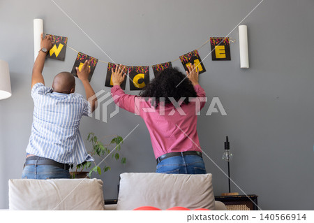 Couple hanging string black cards spelling welcome in yellow on living room wall Couple hanging string black cards spelling welcome in yellow on living room wall 140566914