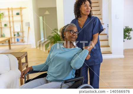 African american caregiver in scrubs assisting patient sitting in wheelchair in living room African american caregiver in scrubs assisting patient sitting in wheelchair in living room 140566976