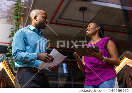 African american coworkers standing on staircase landing reviewing printed documents, tablet African american coworkers standing on staircase landing reviewing printed documents, tablet 140566985