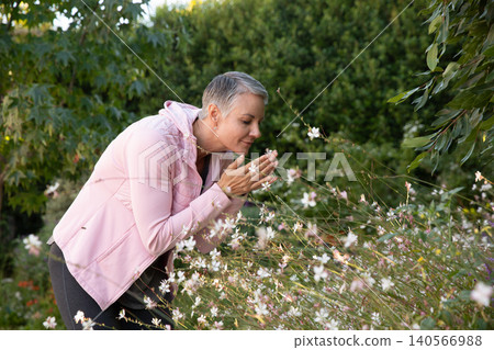 Mature adult woman leaning over wildflowers in backyard garden, cupping blossom next to face Mature adult woman leaning over wildflowers in backyard garden, cupping blossom next to face 140566988