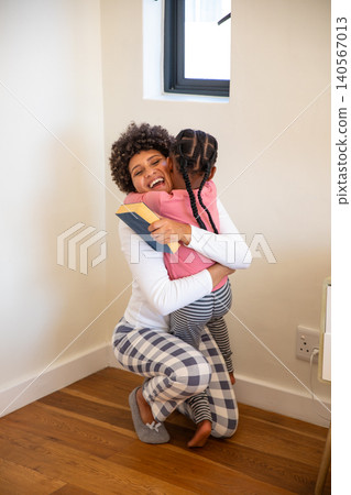 African american mother and daughter kneeling and hugging at home while holding hardcover book African american mother and daughter kneeling and hugging at home while holding hardcover book 140567013
