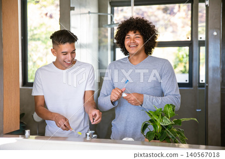 Diverse male friends brushing teeth at bathroom sink with toothbrushes potted plant and windows Diverse male friends brushing teeth at bathroom sink with toothbrushes potted plant and windows 140567018