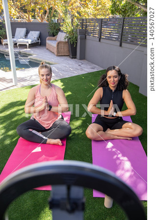 Female friends practicing yoga on backyard patio using ring light smartphone on yoga mats Female friends practicing yoga on backyard patio using ring light smartphone on yoga mats 140567027
