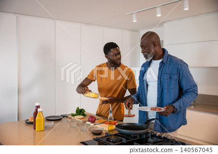 African american father and son cooking breakfast on kitchen island using tongs, frying pan African american father and son cooking breakfast on kitchen island using tongs, frying pan 140567045