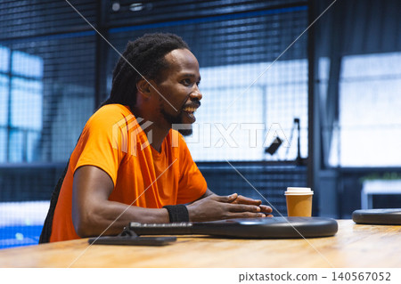 African American man wearing orange shirt leaning on table at sports hall with discs and smartphone African American man wearing orange shirt leaning on table at sports hall with discs and smartphone 140567052