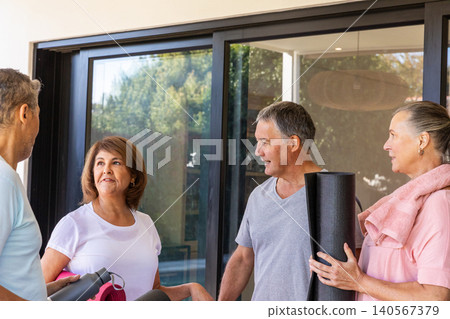 Diverse friends gathering at sliding door on patio in activewear, holding yoga mats, water bottle Diverse friends gathering at sliding door on patio in activewear, holding yoga mats, water bottle 140567379