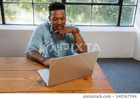 African American adult male sitting in home office at wooden table, working on silver laptop African American adult male sitting in home office at wooden table, working on silver laptop 140567394