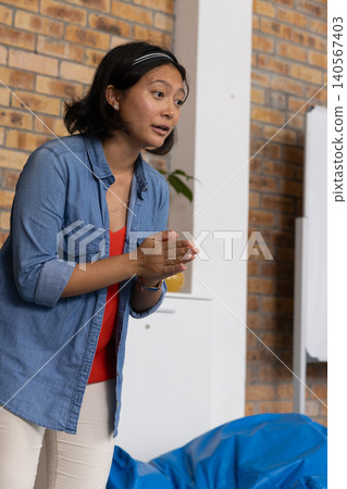 Asian woman leaning forward, gesturing, speaking in meeting room with denim shirt, brick, flipchart Asian woman leaning forward, gesturing, speaking in meeting room with denim shirt, brick, flipchart 140567403