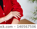 A woman's hands rolling up the sleeves of her red cardigan. 140567506