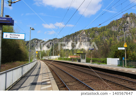 A daytime perspective of railway tracks leading into a picturesque landscape, featuring passenger platforms and signs directing to Sch na and Dresden. A daytime perspective of railway tracks leading into a picturesque landscape, featuring passenger platforms and signs directing to Sch na and Dresden. 140567647