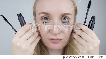 Woman comparing tubing mascara vs regular cosmetics. Woman showing makeup test with smudge proof thermal product on one eye and blurry panda effect on the other. Woman comparing tubing mascara vs regular cosmetics. Woman showing makeup test with smudge proof thermal product on one eye and blurry panda effect on the other. 140568494