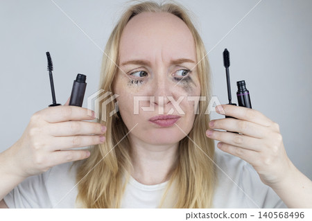 Woman comparing tubing mascara vs regular cosmetics. Woman showing makeup test with smudge proof thermal product on one eye and blurry panda effect on the other. Woman comparing tubing mascara vs regular cosmetics. Woman showing makeup test with smudge proof thermal product on one eye and blurry panda effect on the other. 140568496