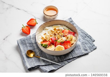 Natural Greek yogurt with granola, banana and strawberries in a bowl on a marble background Natural Greek yogurt with granola, banana and strawberries in a bowl on a marble background 140569338