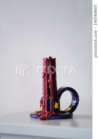 Unlit melted red wax candle in a handmade candle holder Unlit melted red wax candle in a handmade candle holder 140569605