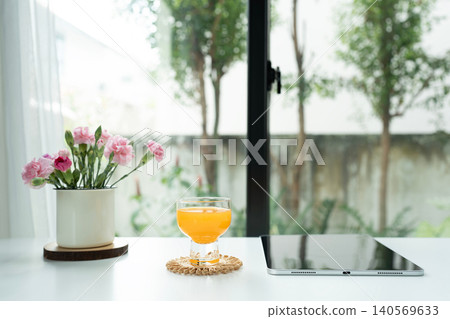 Orange juice in a glass cup and tablet and pink flowers arranged on white desk Orange juice in a glass cup and tablet and pink flowers arranged on white desk 140569633