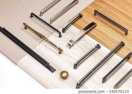 Different types of cabinet handles arranged on surfaces of wood and laminate in a workshop setting Different types of cabinet handles arranged on surfaces of wood and laminate in a workshop setting 140570110