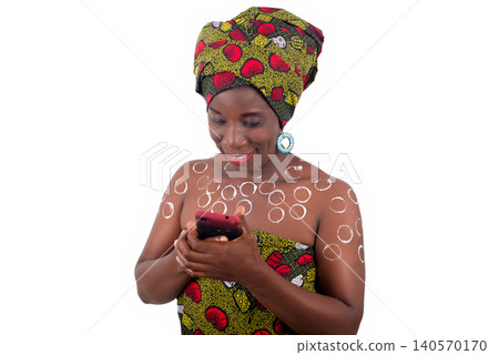 young african woman standing in loincloth in a studio looking at mobile phone smiling. young african woman standing in loincloth in a studio looking at mobile phone smiling. 140570170
