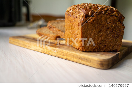 Whole grain loaf with seeds on wooden cutting board in kitchen scene with warm window light Whole grain loaf with seeds on wooden cutting board in kitchen scene with warm window light 140570937