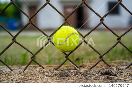 Bright tennis ball stuck in rusty chain link fence with blurred court background 140570947