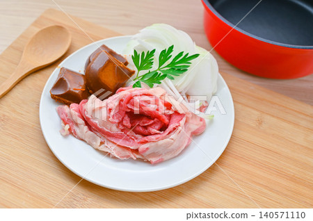 一盤牛肉、洋蔥片、一塊咖哩塊和一個紅色的鍋子。 一盤牛肉、洋蔥片、一塊咖哩塊和一個紅色的鍋子。 140571110